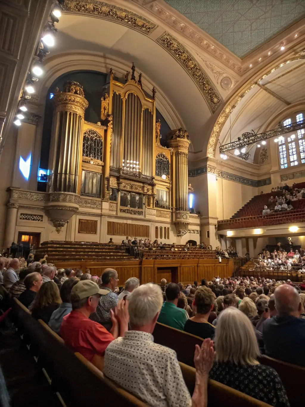 A candid image of a small audience attending a summer evening concert, with an organist performing on a restored harmonium, sunlight streaming through stained glass windows, and community members listening attentively.