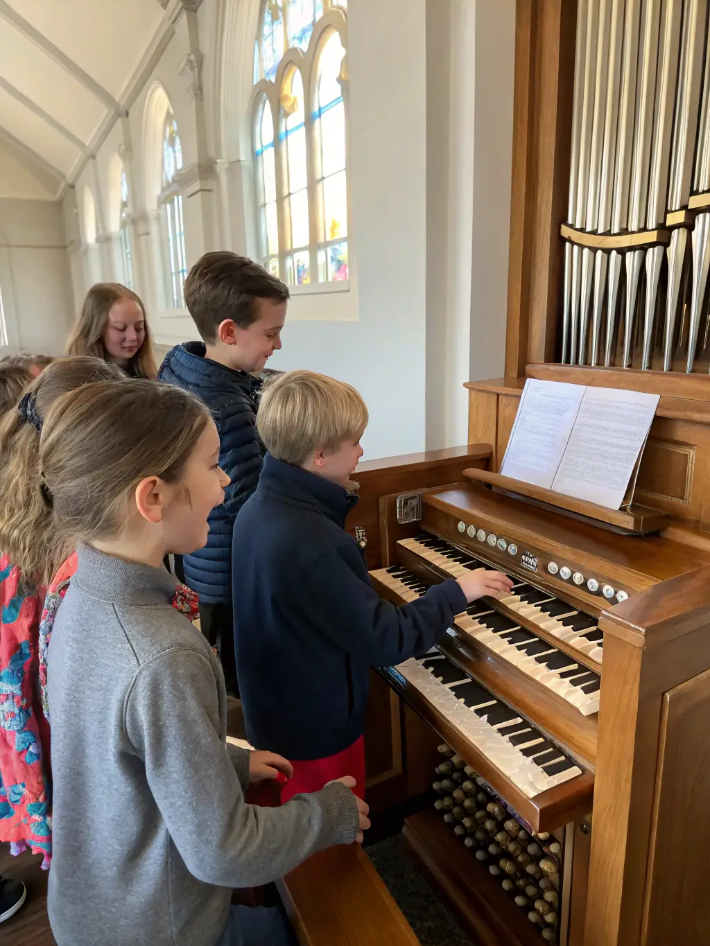 A vibrant photo of children and adults gathered around a historic pipe organ inside a rural church, with a local musician explaining the instrument’s mechanics during an educational workshop organized by LES ORGUES DANS NOS CAMPAGNES.